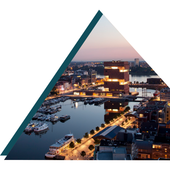 Smart Cities Belgium: Sunset view of Antwerp's MAS museum and harbor area with boats docked along the illuminated promenade.