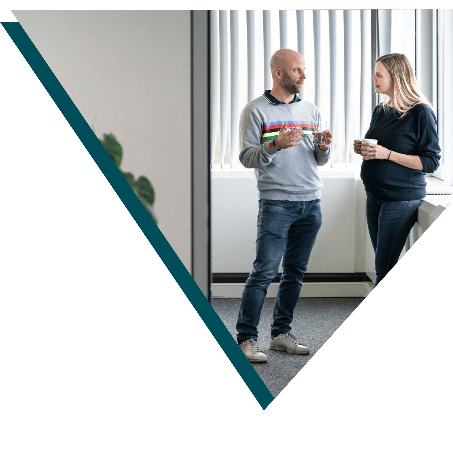 Two Sirus employees standing and having a casual conversation with coffee cups in hand.