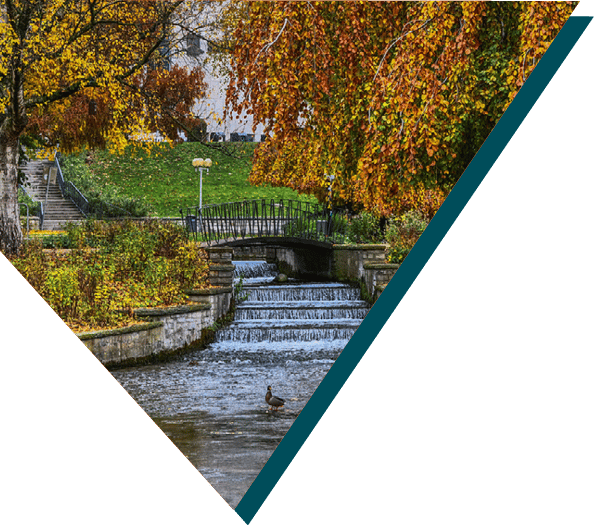 A scenic view of an autumn park in Paderborn featuring a small waterfall, bridge, and vibrant foliage.