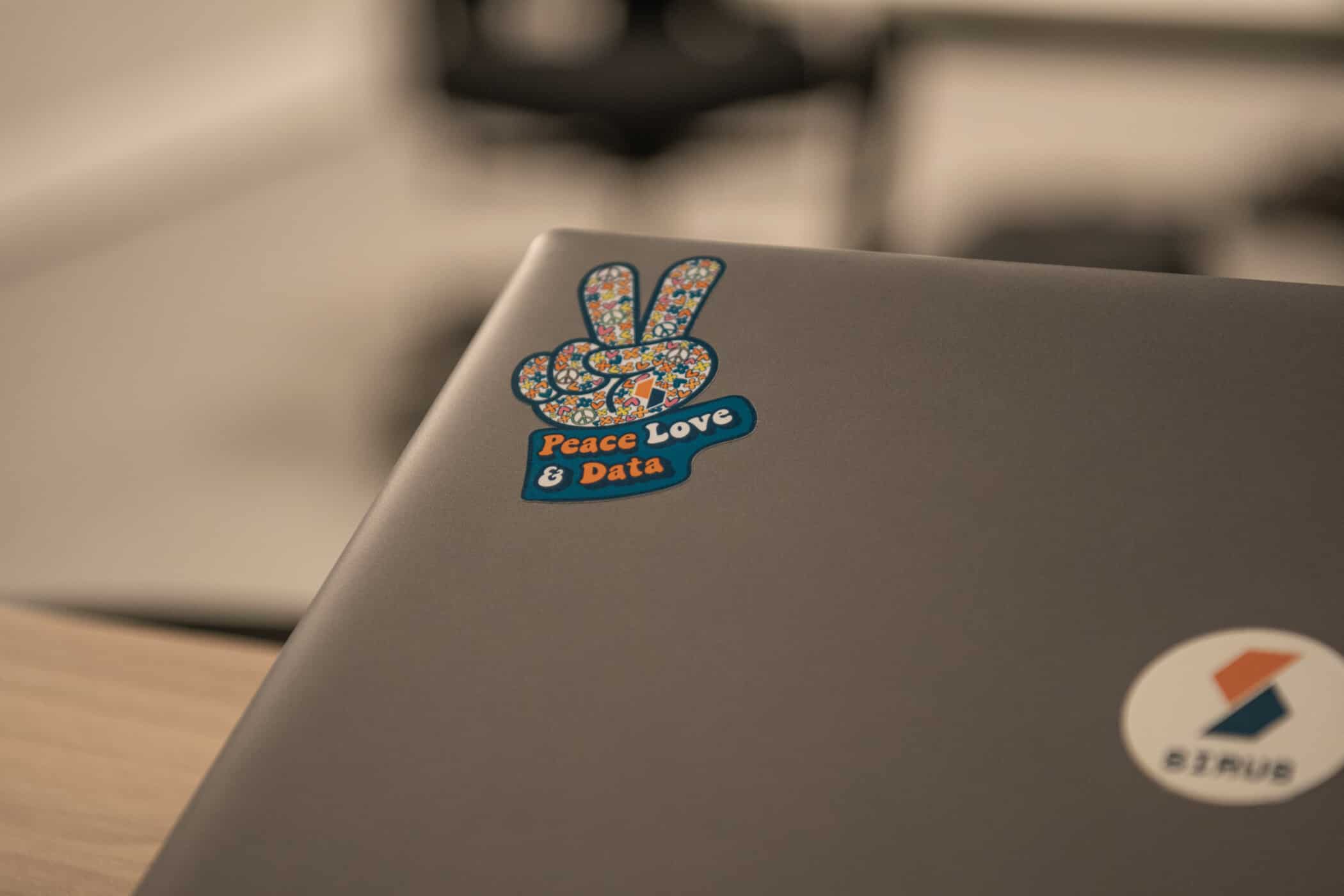 Laptop with "Peace Love & Data" sticker on silver surface in office workspace