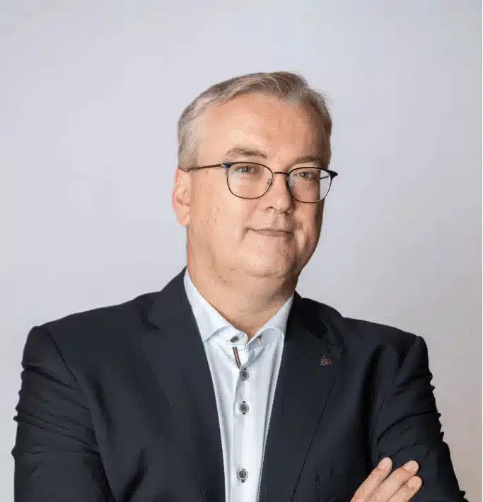 Jan Syssauw of Sirus AI in navy suit with crossed arms and glasses,