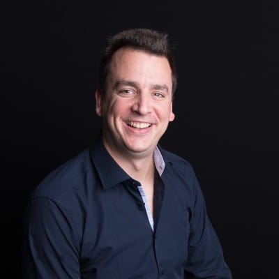 Professional headshot of Robin De Boom, smiling man in navy blue shirt against dark background
