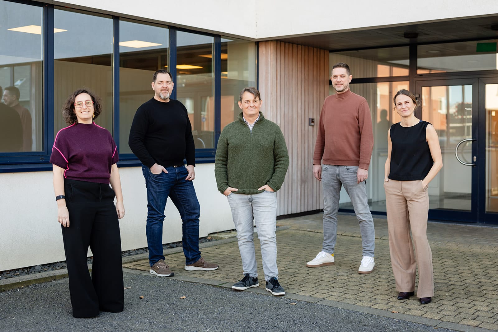 Five Sirus team members standing outside modern office building with glass windows and wood paneling