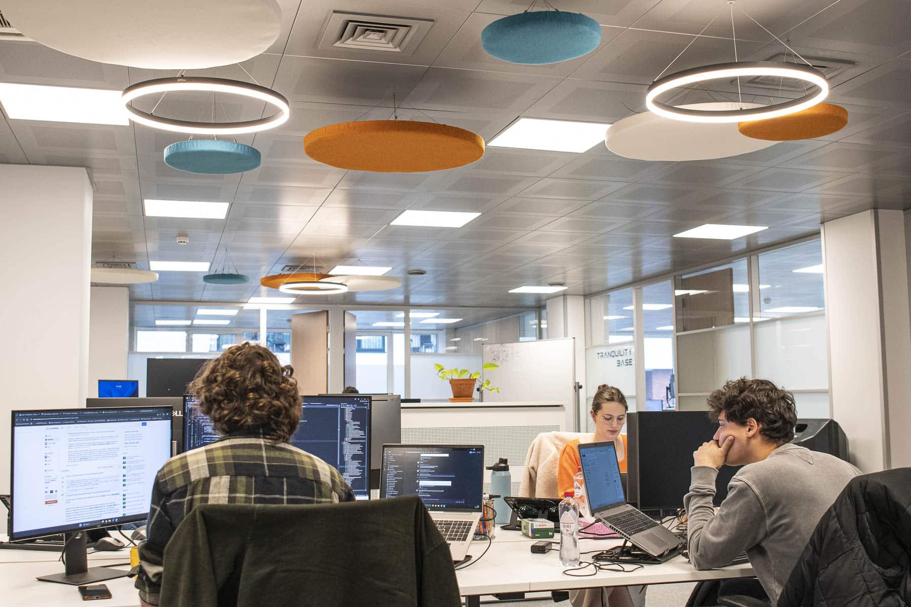 Modern office workspace with developers working at computers under colorful suspended acoustic panels