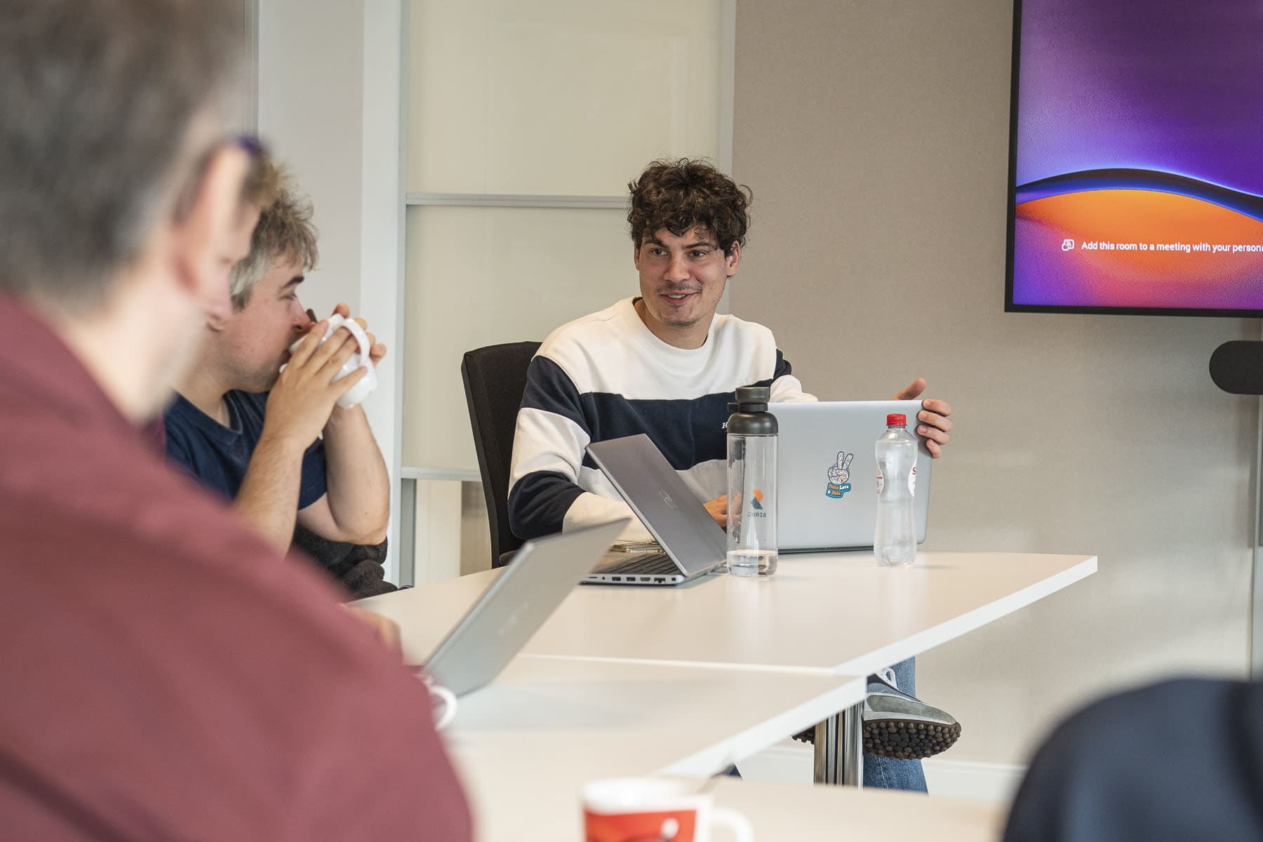 Team meeting at Sirus office with colleagues discussing data solutions around conference table with laptops