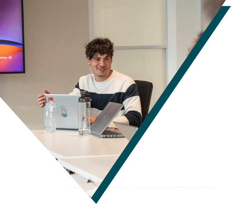 Smiling Sirus developer working on laptop at modern office desk with water bottles and wall-mounted screen