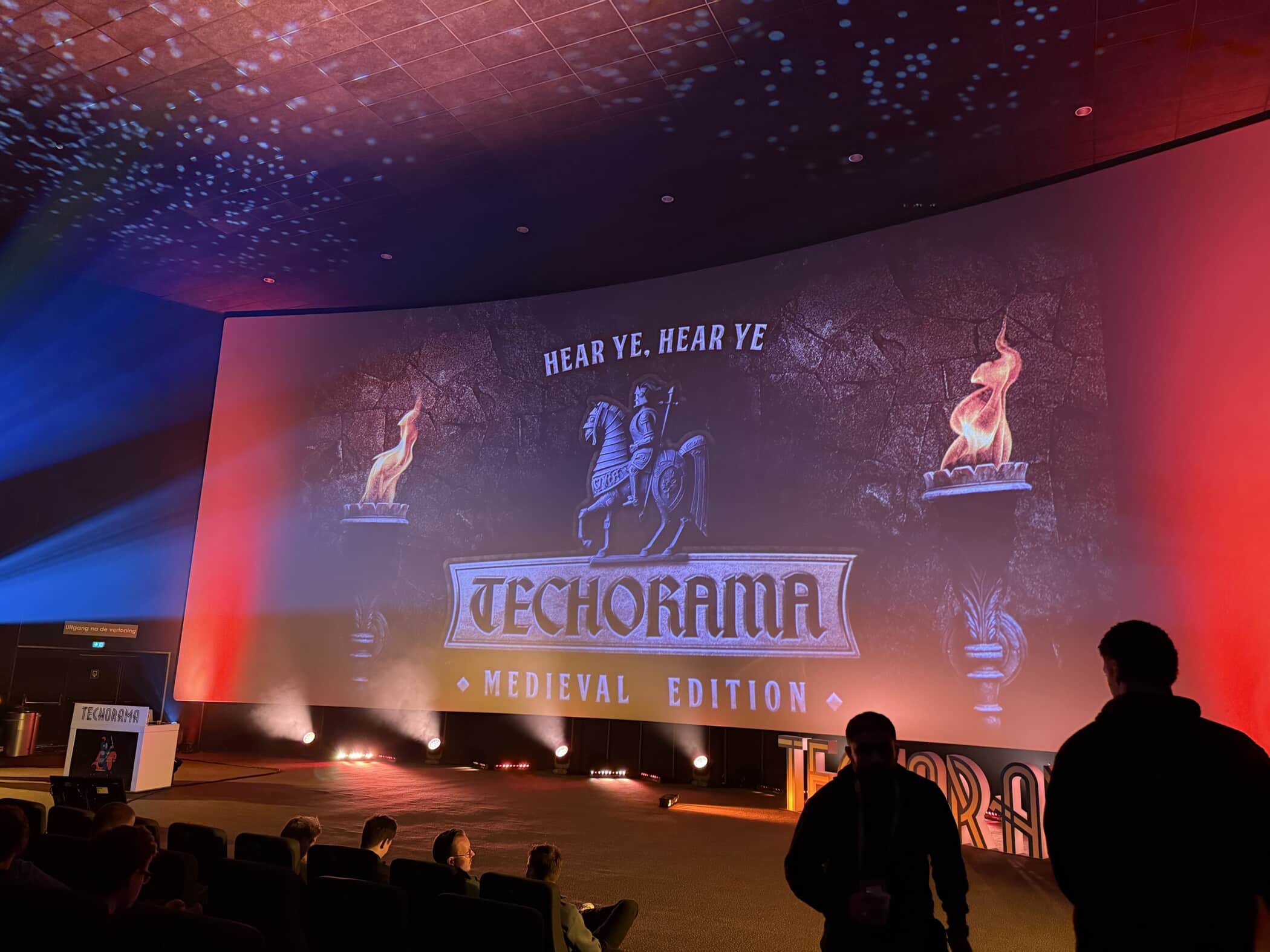 Techorama Medieval Edition conference screen with knight logo and flame torches in auditorium setting