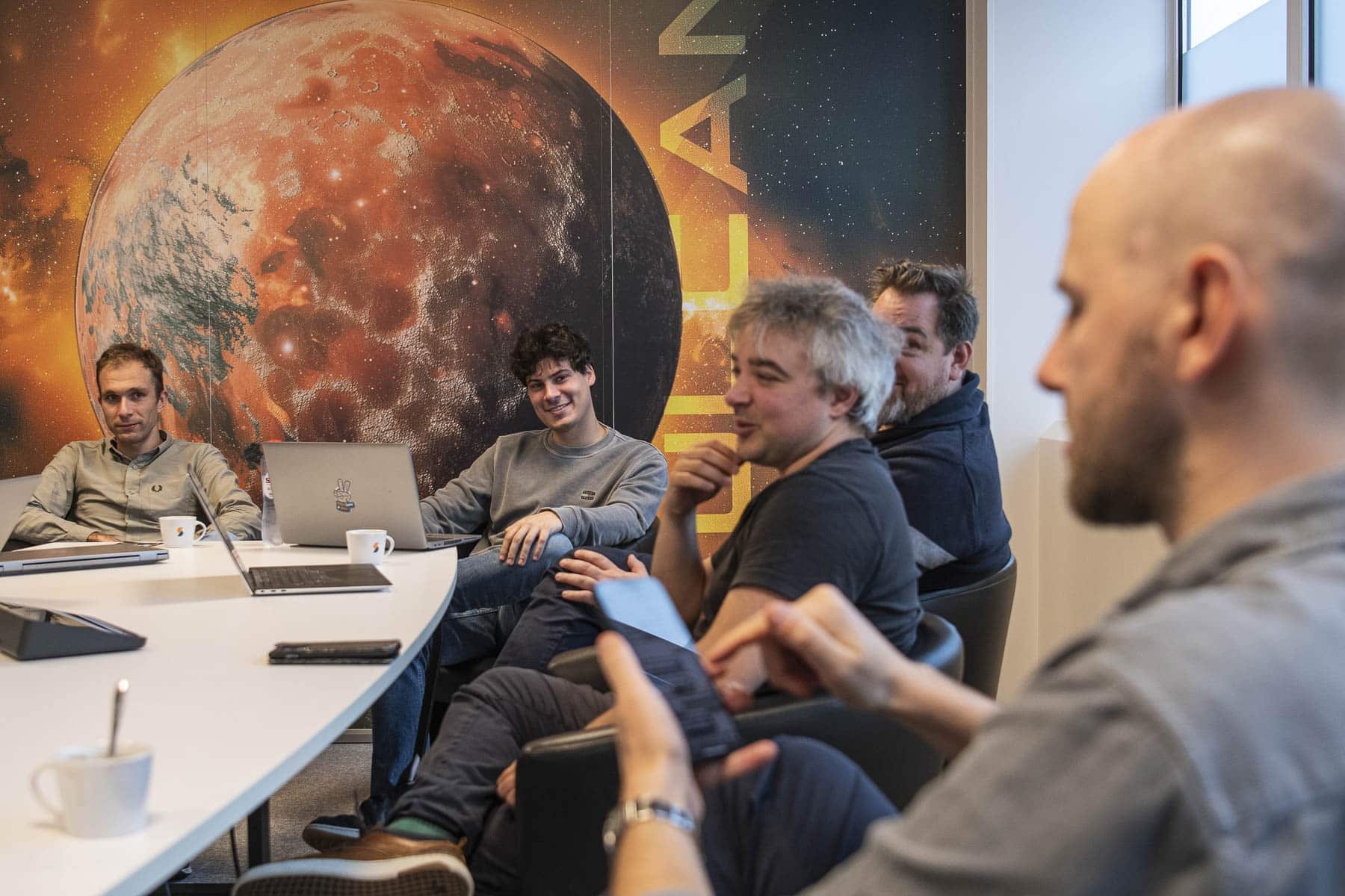Sirus team members in a collaborative meeting, seated around a white table with laptops, in front of a large Mars-themed wall