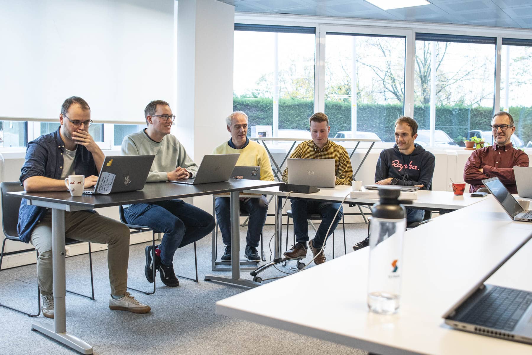 Sirus team members collaborating in a bright office meeting room, each working on laptops at shared tables during a team session